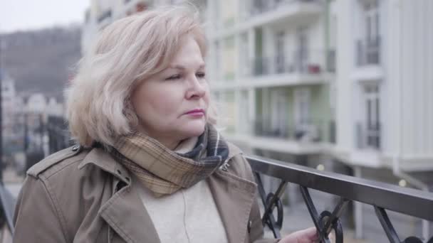 Närbild av ledsna äldre kaukasiska kvinna utomhus. Ensam kvinna pensionär i höst halsduk tittar bort stående på stadens gata. Åldrande, pension, livsstil. — Stockvideo