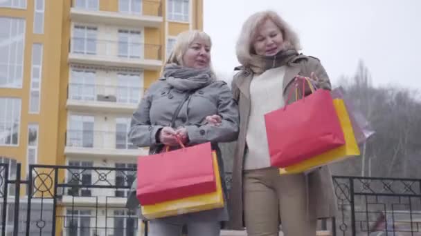 Kaukasiska kvinnor promenerar på stadens gata efter att ha handlat. Glada aktiva medelålders pensionärer som njuter av fritid på pension utomhus. Förmögenhet, shopaholism, hobby, livsstil. — Stockvideo