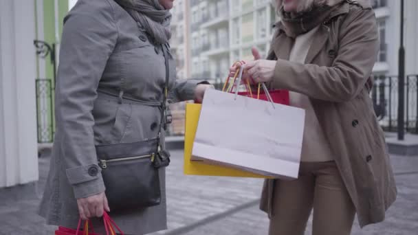 Oigenkännlig kaukasisk mogen kvinna visar inköp till vän och dans på stadens gata. Glad senior pensionärer chatta efter shopping utomhus. Fritid, livsstil, shopaholism, pension. — Stockvideo