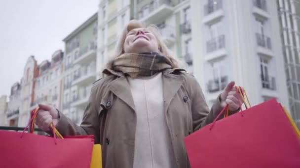 Portret van een opgewonden oudere blanke vrouw die van shopaholisme houdt. Focus verandert van gezicht tot boodschappentassen en terug. Gelukkige vrouwelijke gepensioneerde die rust op pensioen. Lifestyle, vreugde, vrije tijd. — Stockvideo