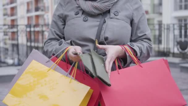 Close-up de mãos caucasianas femininas abrindo carteira vazia. Mulher irreconhecível com sacos de compras fechando bolsa de dinheiro e encolhendo os ombros ao ar livre. Shopaholism, venda, estilo de vida, poupança . — Vídeo de Stock