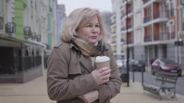 Şehir caddesinde kahve içen kıdemli beyaz kadın. Orta yaşlı emekli, güz gününde dışarıda birini bekliyor. Yaşam tarzı, boş zaman, hava, mevsim. — Stok video