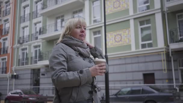 Kendine güveni tam, Kafkasyalı bir kadın şehir caddesinde yürüyor ve kahve içiyor. Rahat kadın emekliler dışarıda vakit geçiriyorlar. Boş zaman, yaşam tarzı, eğlence, emeklilik, turizm. — Stok video