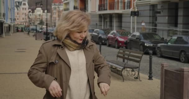 Medelålders vit kvinna tittar på klockan som står på stadens gata. Porträtt av äldre elegant dam som väntar utomhus. Livsstil, möten, pension, fritid. Cinema 4k Prores Hq. — Stockvideo