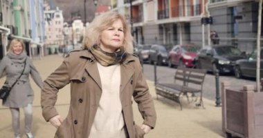 Pozitif kıdemli beyaz kadın arka plandan garsonluğa koşuyor. Neşeli emekliler güneşli bir sonbahar gününde şehir caddesinde buluşuyorlar. Boş zaman, emekli maaşı, mutluluk, yaşam tarzı. Sinema 4k Prores Merkezi.