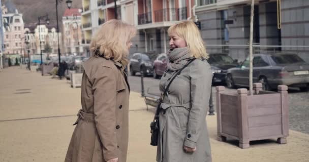 Két vidám idős nő beszélget a város utcáin a napsütéses őszi napon. Pozitív kaukázusi nyugdíjasok, akik a szabadban élvezik a nyugdíjat. A barátok pletykálnak és nevetnek. Szabadidő, életmód. Mozi 4k Prores Hq. — Stock videók