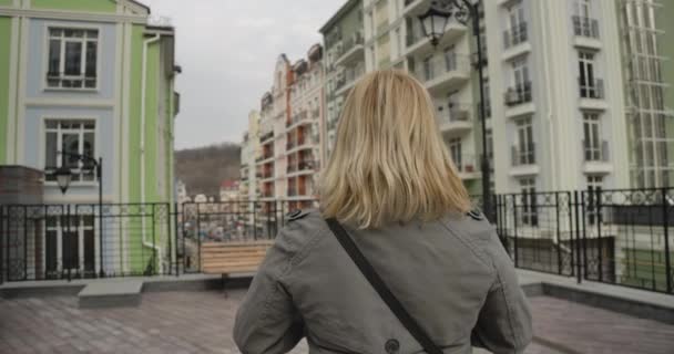 Visszapillantás közeli felvételre egy őszi kabátos szőke nőről, aki a város utcáján áll. Vezető kaukázusi nyugdíjas, aki körbeutazza a világot. Szabadidő, életmód, nyugdíj, boldogság. Mozi 4k Prores Hq. — Stock videók