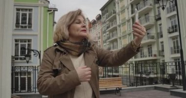 Özçekim kamerasında konuşan ve çevresini gösteren mutlu beyaz emeklinin yakın plan portresi. Yabancı bir ülkede seyahat ederken video kaydeden olumlu bir kadın. Boş zaman, turizm. Sinema 4k Prores Merkezi.