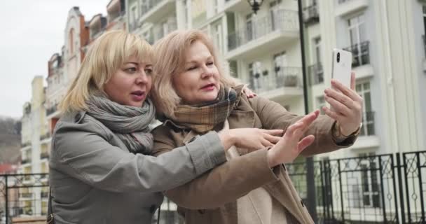 Vidám, kaukázusi idős nők pózolnak szelfi fotókon a szabadban. Pozitív gondtalan nyugdíjasok töltenek szabadidőt a város utcáin. Szabadidő, öröm, boldogság, életstílus. Mozi 4k Prores Hq. — Stock videók