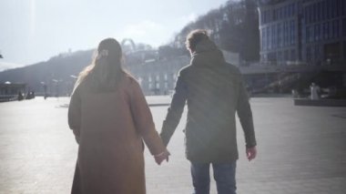 Genç beyaz bir çift dışarıda yürüyüp konuşuyor. Sonbahar şehrinde gezen kadın ve erkeğin arka görüntüsü. Mutlu sevgili, güneşli günün tadını çıkarıyor. Çıkma, ilişki, yaşam tarzı.