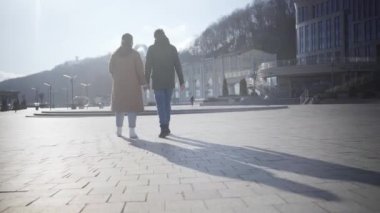 Şehir meydanında gezen mutlu çiftin geniş bir görüntüsü. Güneşli bir sonbahar gününde açık havada yürüyen beyaz kadın ve adamın arka görüntüsü. Romantizm, flört, aşk, birlik.