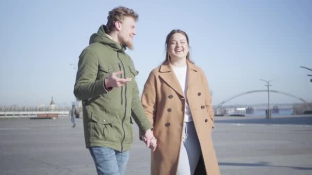 Retrato de un joven hombre y una mujer caucásicos sonrientes hablando como caminando al aire libre. Pareja feliz saliendo en la plaza de la ciudad en un día soleado. Romance, amor, felicidad, estilo de vida . — Vídeos de Stock