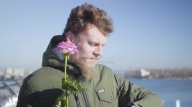 Pembe gül kokan ve saate bakan genç beyaz adamın yakın çekimi. Kızıl saçlı, bıyıklı ve sakallı erkek arkadaşı nehir kıyısında kız arkadaşını bekliyor. Aşk, aşk, yaşam tarzı..