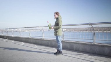 Genç, beyaz, tombul bir kız Rose 'la nehir kıyısında dikilmiş ona sarılıyor. Güneşli bir günde dışarıda çıkan mutlu çiftin yan görüntüsü. Romantizm, yaşam tarzı, aşk, birliktelik.