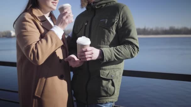 Onherkenbare blanke jongen en meisje praten en drinken buiten koffie. Gelukkig jong stel dat uitgaat op de oever van de rivier op zonnige herfstdag. Vreugde, vrije tijd, levensstijl, liefde. — Stockvideo