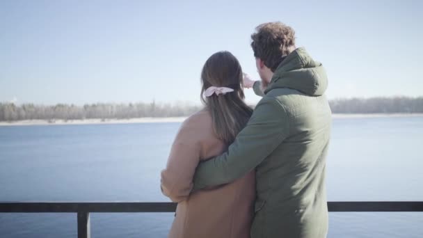 Blick zurück auf ein glückliches junges Paar, das an einem sonnigen Herbsttag am Flussufer plaudert. Kaukasischer Mann umarmt Freundin und zeigt auf etwas weg. Freude, Liebe, Romantik, Lebensstil, Einheit. — Stockvideo