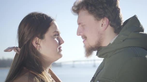 Gros plan de l'homme caucasien souriant avec anneau nasal et femme brune potelée frottant le nez sur la rive de la rivière. Vue latérale de couple heureux amoureux sortir ensemble en plein air. Loisirs, joie, mode de vie, romance . — Video