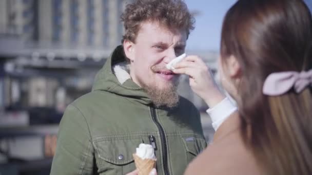 Unrecognizable brunette woman cleaning boyfriends nose dirty with ice cream. Positive young man smiling and looking at girlfriend with love. Shooting over shoulder. Lifestyle, dating, leisure. — Stock Video