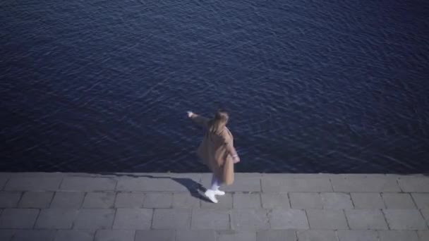 Vue du dessus de joyeuse jeune femme caucasienne tournant sur la rive de la rivière. Plan large de fille joufflue heureuse profitant d'une journée ensoleillée en plein air. Bonheur, mode de vie, joie, loisirs . — Video