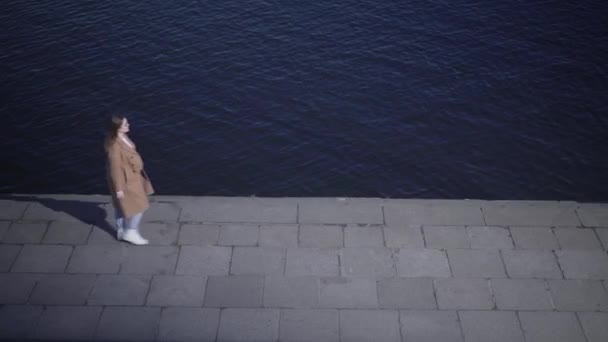 Draufsicht eines jungen kaukasischen Mädchens, das von links nach rechts die Einschiffung des Flusses entlang geht und geht. Eine erwachsene Frau im Herbstmantel schlendert im Freien. Freizeit, Lifestyle, Natur. — Stockvideo