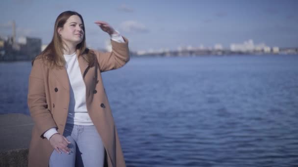 Portrait of brunette Caucasian chubby girl looking away and holding hand on forehead. Happy woman resting on the bank of river on sunny day. Lifestyle, joy, leisure. — Stock Video