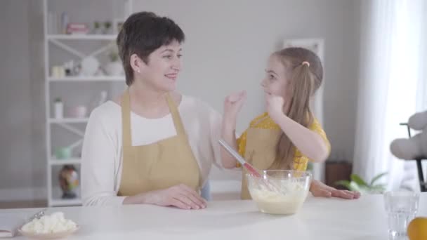 Cute positive girl giving high five to grandmother at kitchen, happy woman hugging granddaughter. Caucasian family baking pancakes for Shrove Tuesday. Lifestyle, cooking, Shrovetide. — Stock Video