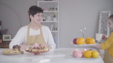 Güzel küçük kız, masaya fırında kreplerle fincanlar getiriyor. Önlüklü mutlu büyükanne ve torun yemek yaptıktan sonra tatlıyla çay içiyor. Shrove Salı, birlik, yaşam tarzı.