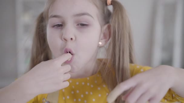 Gros plan d'une petite fille heureuse dégustant un mélange sucré pour la boulangerie à partir des doigts. Souriant mignon enfant caucasien crêpes à pâtisserie pour Shrove Tuesday. Mode de vie, joie, Shrovetide . — Video