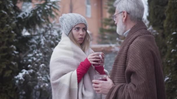 Retrato de una joven hermosa mujer caucásica bebiendo té al aire libre con un hombre de pelo gris. Chica sonriente y jubilado mayor disfrutando del día de invierno. Estilo de vida, ocio, felicidad . — Vídeos de Stock