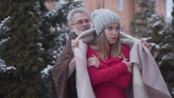 Homem caucasiano bonito sênior cobrindo jovem mulher com cobertor. Retrato de casal feliz com diferença de idade desfrutando de dia de inverno ao ar livre. Lazer, estilo de vida, amor, romance . — Vídeo de Stock