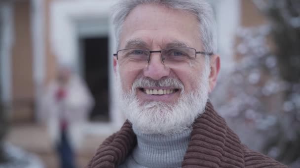 Gros plan sur le visage d'un bel homme gracieux aux lunettes souriant à la caméra. Retraité caucasien aux cheveux gris âgé posant à l'extérieur le jour de l'hiver. Mode de vie, loisirs, détente . — Video