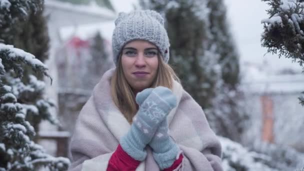 Retrato de la joven mujer caucásica feliz en sombrero de invierno y guantes de pie al aire libre. Sonriente dama encantadora posando en el fondo de árboles de piel verde. Estilo de vida, belleza, ocio, alegría . — Vídeo de stock