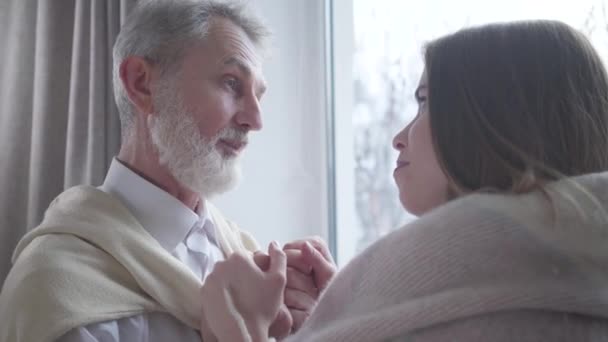 Portrait d'un homme caucasien âgé excité amoureux parlant à une jeune femme souriante à l'intérieur. Positif retraité aux cheveux gris bavardant avec une fille aimante. Amour, différence d'âge, unité, style de vie . — Video