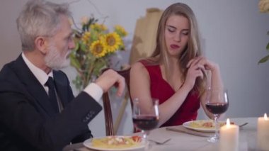 Genç, güzel, beyaz bir kadın romantik bir akşam yemeğinde beyaz saçlı bir adamı baştan çıkarıyor. Kırmızı elbiseli esmer kız takım elbiseli kıdemli iş adamına aşkla bakıyor. Yaşam tarzı, romantizm, keyif.