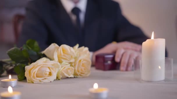 Букет желтых роз, лежащих на столе со свечами, стоящими вокруг. Неузнаваемый человек в костюме время проверки на часы и глядя в подарочную коробку с обручальным кольцом. Любовь, романтика, предложение о браке — стоковое видео