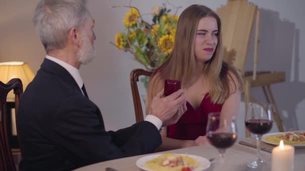 Young annoyed Caucasian woman laughing at senior man presenting her wedding ring and refusing to get married. Portrait of beautiful girl in red dress saying no to loving guy. Relationship difficulties — Stock Video
