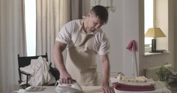 Retrato do jovem caucasiano diligente que passa completamente a roupa de cama em casa. Bonito morena cara usando eletrodomésticos em casa. Estilo de vida, serviço de limpeza, rotina. Cinema 4k ProRes HQ . — Vídeo de Stock