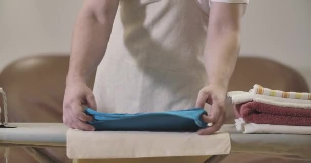 Male Caucasian hands folding laundry on ironing board. Unrecognizable young man doing housework at home. Lifestyle, housekeeping, routine, cleanliness. Cinema 4k ProRes HQ. — Stock Video