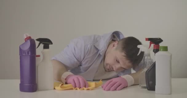 Diligente joven caucásico frotando mesa blanca con agente limpiador. Hombre adulto ama de llaves en guantes de protección de limpieza de muebles en interiores. Trabajo doméstico, estilo de vida, higiene. Sede del cine 4k ProRes . — Vídeos de Stock