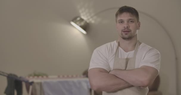 Brunette Caucasian man with brown eyes standing with hands crossed at the background of dryer indoors. Portrait of confident male housekeeper posing at home. Household. Cinema 4k ProRes HQ. — Stock Video