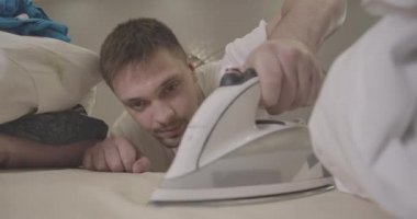 Genç, kendine güvenen beyaz bir adam içeride kıyafetlerini ütülüyor. Ev işi yapan esmer, yakışıklı adamın portresi. Kişinin yüzüne odaklanmış. Oda servisi, yaşam tarzı, ev işleri. Sinema 4k Prores Merkezi.