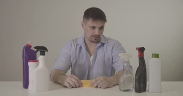 Retrato de un hombre guapo mirando detergentes en la mesa y tirando todo. Joven caucásico morena chico cansado de tareas domésticas y limpieza. Estilo de vida, limpieza. Sede del cine 4k ProRes . — Vídeo de stock