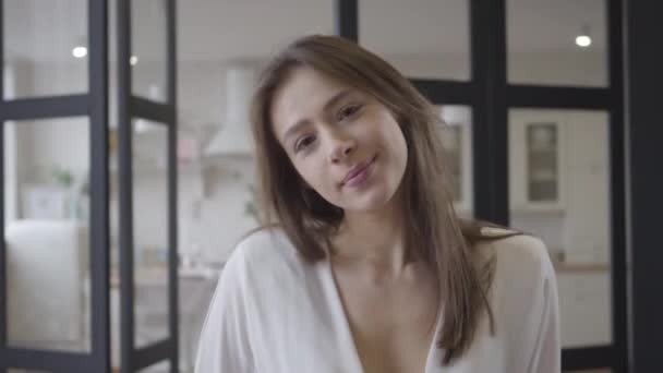 Retrato de cerca de una mujer caucásica morena de ojos marrones sonriendo a la cámara. Encantadora jovencita posando en casa. Ocio, belleza, estilo de vida, felicidad . — Vídeos de Stock