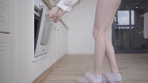 Felnőtt szexi kaukázusi nő kinyitja a sütőt a konyhában, és beteszi a fejét. Barna lány, aki reggelente ételt keres otthon. Életmód, szabadidő. — Stock videók