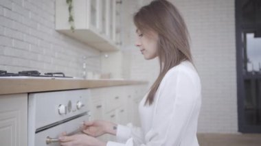 Fırını açıp içine bakan esmer, beyaz bir kadın. Sabahları evde mutfak hizmetlerini kontrol eden hoş bir kadın. Yaşam tarzı, yemek pişirme, boş zaman.