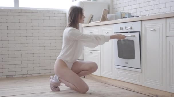 Retrato de vista lateral de una sensual joven mirando dentro del horno en la cocina. Morena chica caucásica en cuerpo blanco utilizando la utilidad de cocina en la mañana. Estilo de vida, belleza, alimentos . — Vídeos de Stock