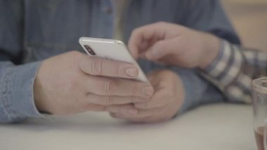 Genç bir adamın ekranı araklarken akıllı telefonu tuttuğu son derece yakın plan beyaz erkek. Yetişkin bir çocuğun modern teknolojiyi olgun bir babaya göstermesi tanınmaz hale geldi. Yaşam biçimi.