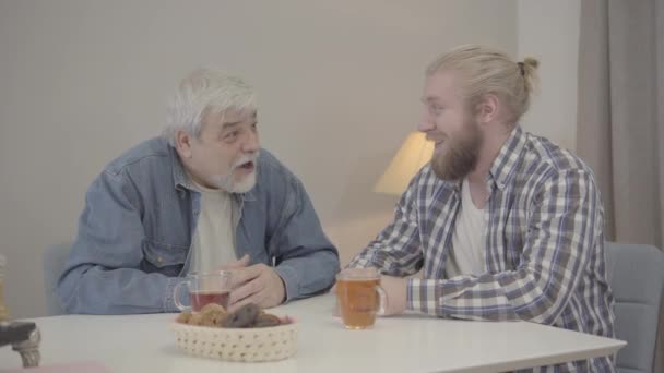 Hombre caucásico de edad avanzada positiva que toma la oreja de hijo adulto y agita el dedo. Alegre jubilado masculino divirtiéndose con chico joven en el interior. Alegría, diversión, estilo de vida, ocio . — Vídeos de Stock