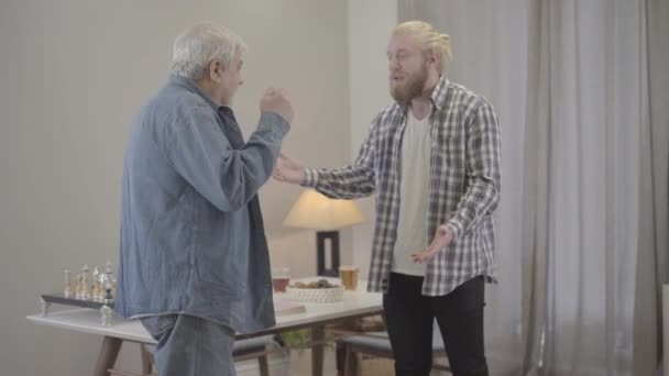 Starszy biały mężczyzna kłóci się z dorosłym synem w domu. Dojrzały emeryt i młody mężczyzna gestykulujący i wrzeszczący w środku. Konflikt, styl życia, rodzina, związek. — Wideo stockowe