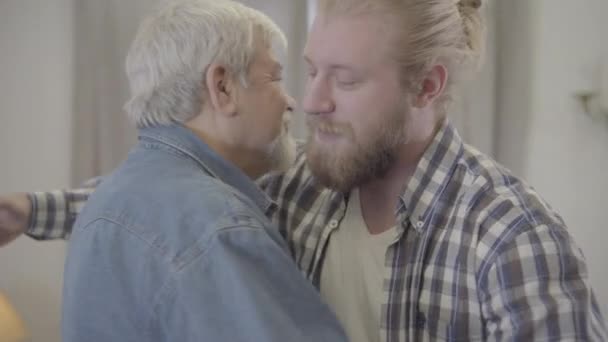 Close-up portrait of adult Caucasian man hugging senior grey-haired father indoors. Happy son and mature retiree smiling. Unity, family relationship, lifestyle. — Stock Video